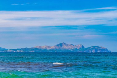 İspanya 'nın Mallorca adasındaki Can Picafort adasında turkuaz su dalgaları ve dağlarla pürüzlü doğal kıyı ve sahil manzarası.