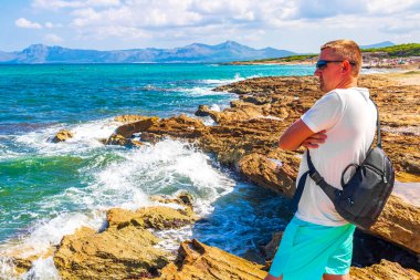 Erkek gezgin ve turist, İspanya 'nın Balear Adası Mallorca' daki Can Picafort 'ta turkuaz su dalgaları, kaya parçaları ve deniz manzarası manzarasını izliyor..