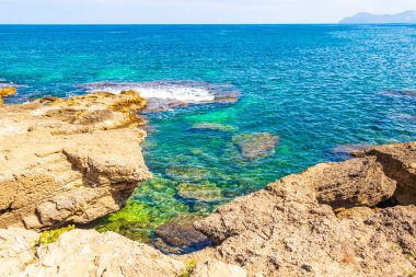 İspanya 'nın Mallorca adasındaki Can Picafort adasında turkuaz su dalgaları, kayalar ve taşlar ile pürüzlü doğal kıyı ve sahil manzarası.
