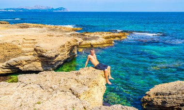 Erkek gezgin ve turist, İspanya 'nın Balearic Adası Mallorca' daki Can Picafort 'ta turkuaz su dalgaları ve kaya parçalarıyla engebeli doğal kıyı ve sahil manzarasında poz veriyor..