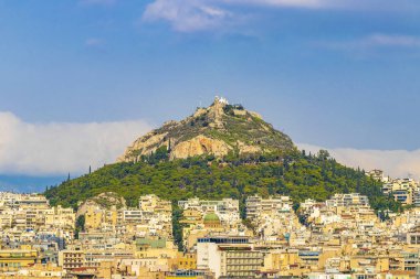 Likavittou Lykabettus and the Holy Church of Saint Isidore with blue cloudy sky in Greece's capital Athens in Greece. clipart