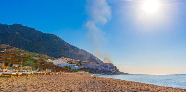 Oros Dikaios Dağları 'nın altında güneş pansiyonları ve şemsiyelerle lüks tatil beldeleri ve plajların üzerinde gün doğumu ve duman. Kos Adası Yunanistan' ın mavi gökyüzü ile doğal kıyı manzaraları.