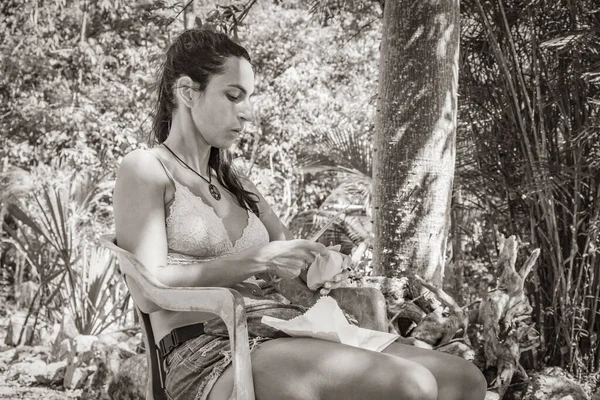 Old black and white picture of Beautiful pretty woman eats mango in the tropical jungle forest plants palm trees at Santuario de los guerreros in Puerto Aventuras Quintana Roo Mexico.