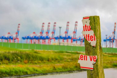 Industrial area cranes and red tower lighthouse with beautiful grassland and dike dyke nature seascape panorama in Imsum Geestland Cuxhaven Lower Saxony Germany.