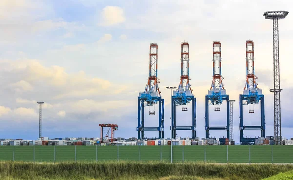 Industrial area cranes and red tower lighthouse with beautiful grassland and dike dyke nature seascape panorama in Imsum Geestland Cuxhaven Lower Saxony Germany.