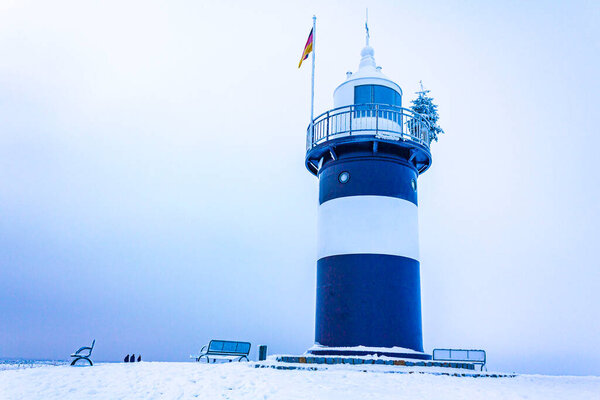Light house at frozen lake river sea on dike with broken snow ice floes black ice with gloomy atmosphere in cold winter in Wremen Cuxhaven Lower Saxony Germany.