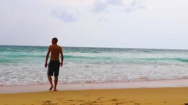 Erkek turist, Thalang Phuket Tayland 'daki turkuaz berrak suyla Nai Thon Naithon Sahili koyunda koşuyor ve yüzüyor.