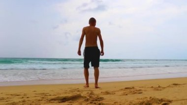Erkek turist, Thalang Phuket Tayland 'daki turkuaz berrak suyla Nai Thon Naithon Sahili koyunda koşuyor ve yüzüyor.