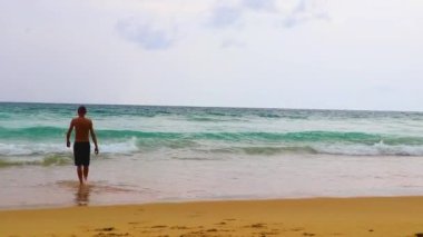Erkek turist, Thalang Phuket Tayland 'daki turkuaz berrak suyla Nai Thon Naithon Sahili koyunda koşuyor ve yüzüyor.