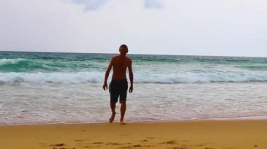 Erkek turist, Thalang Phuket Tayland 'daki turkuaz berrak suyla Nai Thon Naithon Sahili koyunda koşuyor ve yüzüyor.