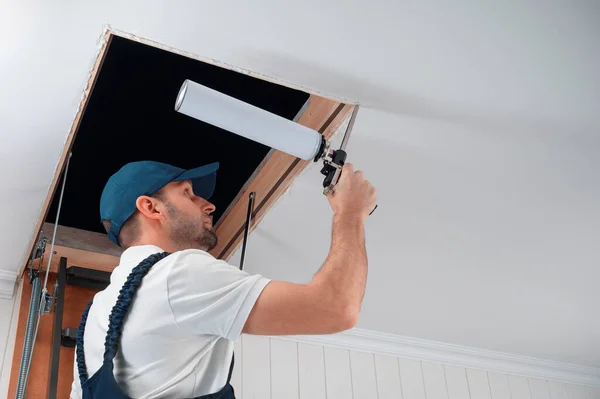 a uniformed specialist fills the gap between the door frame of the attic staircase and the mounting box with polyurethane foam.