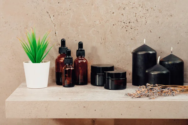 SPA tedavileri ve kokulu mumlar küçük bir saksı bitkisiyle birlikte koyu kahverengi çiçeklerin arasında duruyor. Çevre dostu ürünlerden Aromaterapi vücut bakım ürünleri.