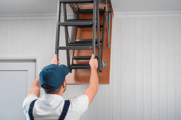 a specialist in uniform folds the attic ladder after installation.