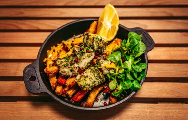 Morina balığı, patates kızartması, limon, fesleğen ve diğer malzemeler siyah tabakta - ahşap zemin.