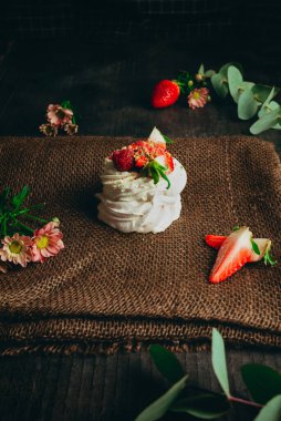 Mini Pavlova kremalı ve koyu arkaplanlı taze çilekli kremalı pastasının kırsal fotoğrafı. Küçük beyaz taze tatlı.. 