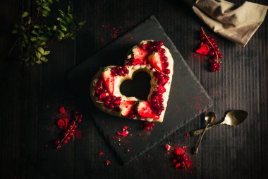 Şekerleme konsepti - siyah tabakta Sevgililer Günü için kalp şeklinde kırmızı ve beyaz pasta. Tatlı ve romantik hediye - Koyu siyah arka planda çilekli kek.