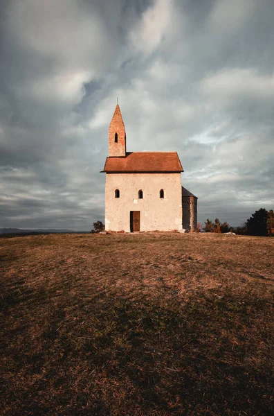 Günbatımında karanlık bulutlu gökyüzü olan Aziz Michael Katolik Kilisesi 'nin dikey fotoğrafı - Drazovce, Slovakya. 
