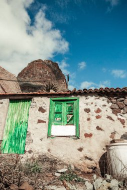 Old typical house in Tenerife - Canary Islands in Masca Village. House with green window with  peak of mountain and blue cloudy sky on background.