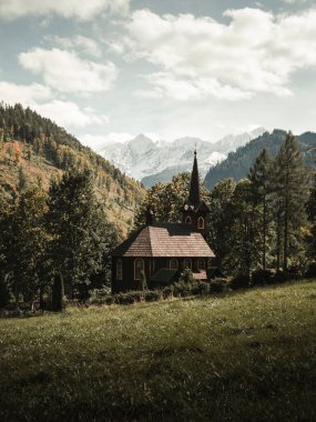 Tatranska Javorina 'daki ahşap kilise arkasında güzel karlı dağlar olan Slovakya. Tepelerin altında yeşil çimen zeminli ahşap şapelin dikey manzara fotoğrafı..