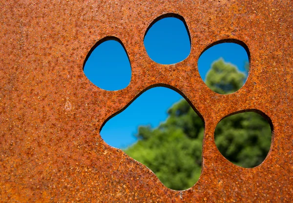 Silhouette of a cat paw in rusty metal wall in front of trees — Stock Photo, Image