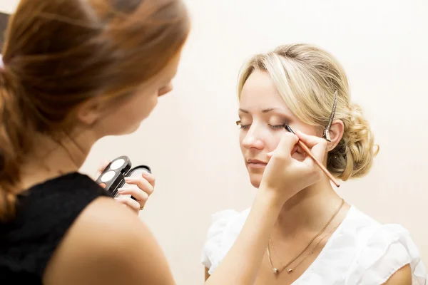 Femme appliquant maquillage pour une mariée dans son jour de mariage près du miroir — Photo