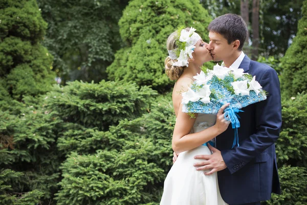 Young couple kissing in wedding gown. Bride holding bouquet with white lilies — Stock Photo, Image