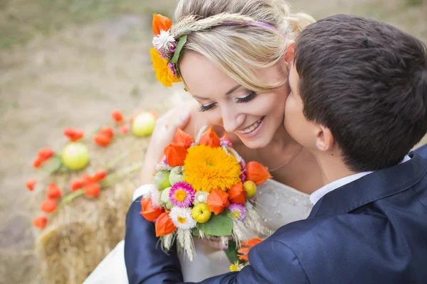 Young couple kissing in wedding gown. Bride holding bouquet of flowers — Stock Photo, Image