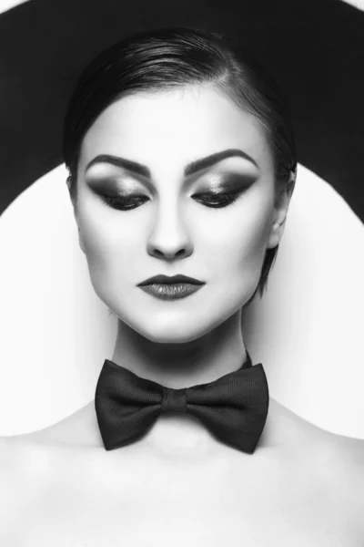 Mujer bonita con maquillaje de noche y labios rojos en una pajarita en el centro de un fondo de diana. Blanco y negro —  Fotos de Stock