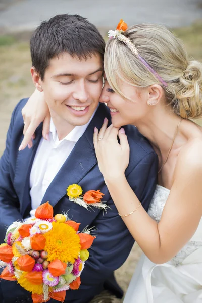 Молода пара цілується у весільній сукні. Наречена тримає букет квітів — стокове фото