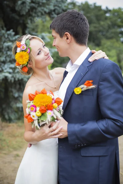 คู่รักหนุ่มสาวจูบกันในชุดแต่งงาน เจ้าสาวถือช่อดอกไม้ — ภาพถ่ายสต็อก