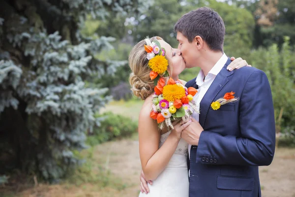 युवा जोड़े शादी के पोशाक में चुंबन। दुल्हन फूलों का गुच्छ पकड़े हुए — स्टॉक फ़ोटो, इमेज