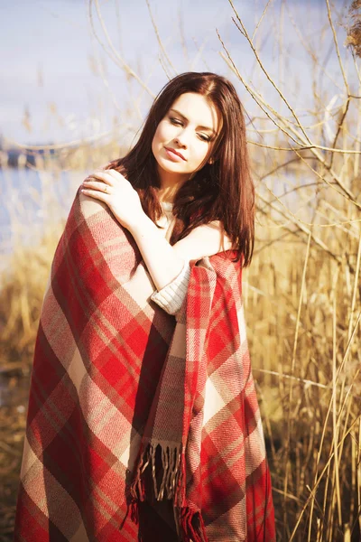 Brunette woman outdoors in check pattern plaid drinking tea and looking down near the lake — Stock Photo, Image