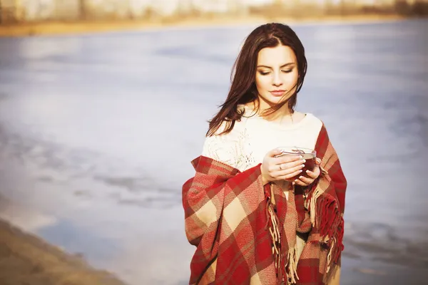 Брюнетка жінку на вулиці в Реєстрація візерунок plaid пити чай і, дивлячись біля озера. копія простір — стокове фото