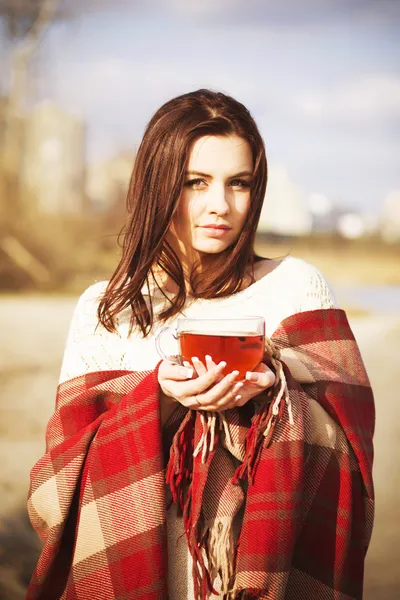 Brunette woman outdoors in check pattern plaid drinking tea and looking down near the lake — Stock Photo, Image