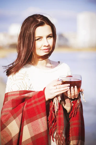 Brunette woman outdoors in check pattern plaid drinking tea and looking down near the lake — Stock Photo, Image