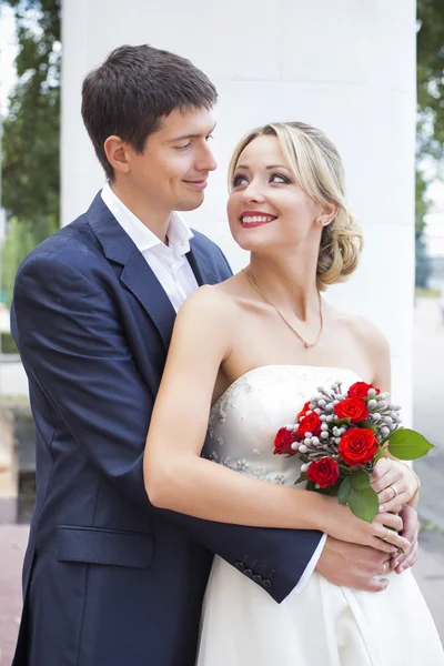 Junges Paar küsst sich im Brautkleid. Braut hält Strauß mit roten Rosen — Stockfoto