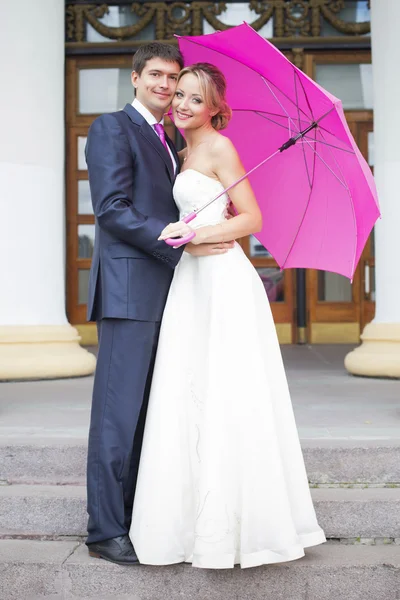 Giovane coppia abbracci in abito da sposa con ombrello rosa — Foto Stock