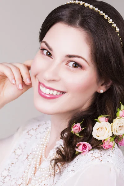 Schöne brünette Braut lächelnd mit natürlichem Make-up und Blumen Rosen in ihrer Frisur und Blick in die Kamera — Stockfoto