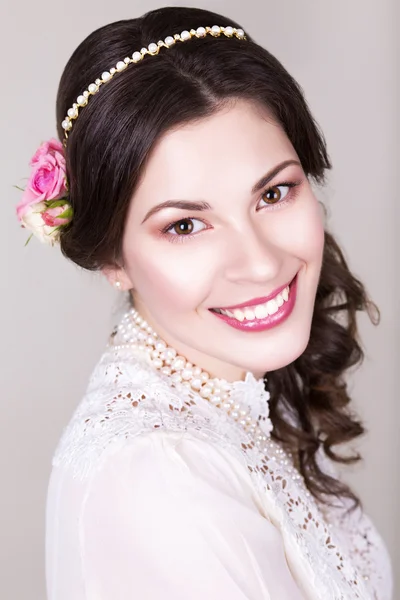 Hermosa novia morena sonriendo con maquillaje natural y flores rosas en su peinado y mirando a la cámara —  Fotos de Stock