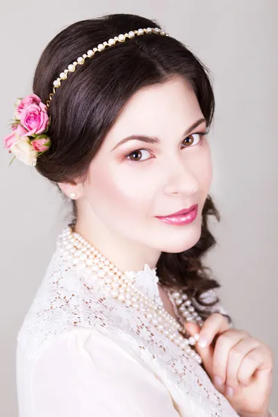 Hermosa novia morena sonriendo con maquillaje natural y flores rosas en su peinado y mirando a la cámara —  Fotos de Stock