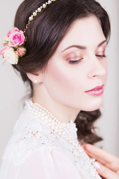 Hermosa novia morena sonriendo con maquillaje natural y flores rosas en su peinado y mirando hacia los lados — Foto de Stock