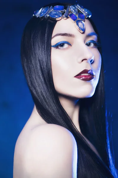 Vacker kvinna från en saga med smycken på hennes hår och händer i en spotlight med blå bakgrundsbelysning tittar på kameran — Stockfoto