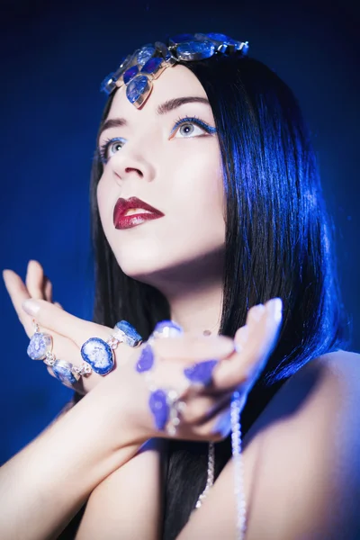 Beautiful woman from a fairytale with a hair horns and jewelry in a spotlight with blue backlight looking at camera — Stock Photo, Image