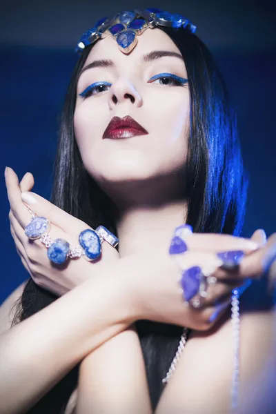 Hermosa mujer de un cuento de hadas con joyas en el pelo y las manos en un centro de atención con la luz de fondo azul mirando a la cámara —  Fotos de Stock