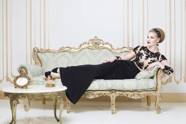 Mooie blonde koninklijke vrouw liggend op een retro bank in prachtige luxe jurk. Binnenshuis. Kopieer ruimte. — Stockfoto