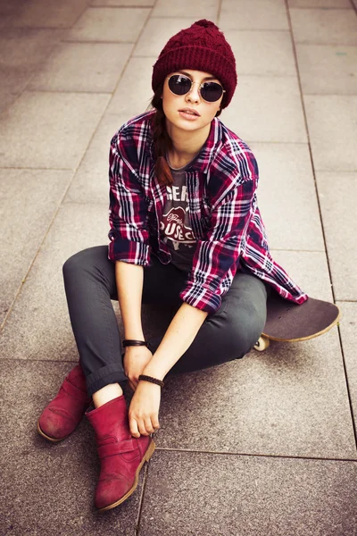Brunett kvinna i hipster outfit sitter på en scateboard på gatan. tonas bild — Stockfoto