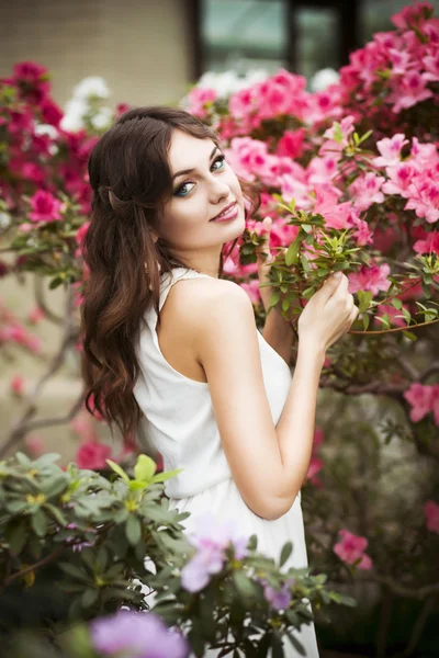 一个美丽的黑发女人，在粉红色的连衣裙和多彩的画像中弥补的户外杜鹃花园 — 图库照片