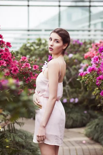 Portret van een mooie brunette vrouw in roze jurk en kleurrijke make-up buitenshuis in azalea tuin — Stockfoto