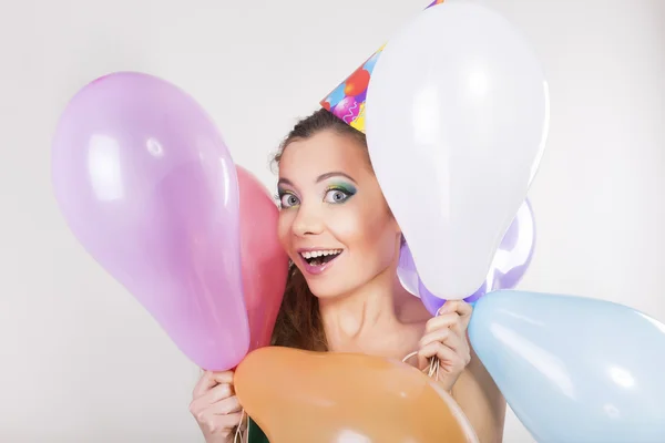 Brunette vrouw in een verjaardag cap bedrijf ballonnen en gelukkig glimlach — Stockfoto