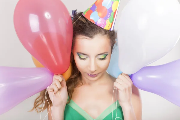 Brunette vrouw in een verjaardag cap bedrijf ballonnen en gelukkig glimlach — Stockfoto